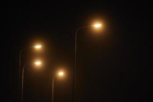 notte lampione brilla con svenire misterioso giallo leggero attraverso sera nebbia a silenzioso città notte foto