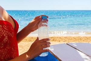 donna mani apertura un' bottiglia di acqua all'aperto su il spiaggia foto