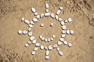 sole con un' Sorridi fatto con pietre su sabbia foto