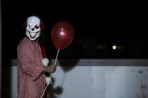 asiatico bello uomo indossare clown maschera con arma a il notte scena, halloween Festival concetto, orrore pauroso foto di un' uccisore nel arancia stoffa, male clown charactor