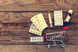 shopping carrello con pillole, siringa su il vecchio legna sfondo. tonica Immagine. foto