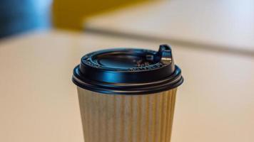 caldo caffè nel Marrone carta tazza, caffè nel bianca scrivania, porta via caffè nel bar negozio, su sfocatura sfondo foto