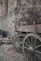 vecchio di legno carrello nel davanti di un vecchio pietra parete nel il villaggio. parcheggiata di legno carrello, tradizionale rurale trasporto, storico oggetti, antico di legno carro ruote. foto