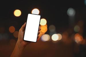 mano Tenere smartphone con vuoto schermo a notte su bokeh città strada sfondo foto