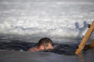 un' uomo tuffa in un buco nel ghiaccio durante il inverno Festival di il battesimo di Gesù. un' uomo nuotate nel il buco nel ghiaccio nel inverno. tricheco le persone. foto