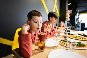 quattro bambini mangiare italiano Pizza nel pizzeria. bambini mangiare a bar. ragazzo bevanda succo. foto