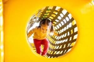 poco ragazza mossa su nel tubo a giallo terreno di gioco parco nel attivo divertimenti. foto