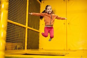 poco ragazza ragazzo salto su trampolino a giallo terreno di gioco parco. bambino nel movimento durante attivo divertimenti. foto