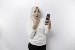 scioccato asiatico donna indossare foulard, Tenere sua Telefono, isolato di bianca sfondo foto