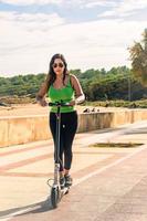 giovane latino ragazza su elettrico scooter avendo divertimento su città strada su un' soleggiato estate giorno. all'aperto ritratto ragazza equitazione elettrico scooter nel il parco. foto