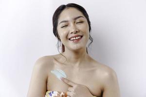 pelle cura prodotti concetto. asiatico donna l'applicazione idratante lozione su corpo dopo doccia, in piedi avvolto nel asciugamano, ritagliata Immagine foto