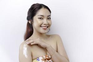pelle cura prodotti concetto. asiatico donna l'applicazione idratante lozione su corpo dopo doccia, in piedi avvolto nel asciugamano, ritagliata Immagine foto