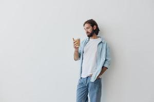libero professionista del Millennio uomo con un' barba potabile caffè a partire dal un' riciclato tazza nel elegante fricchettone Abiti bianca maglietta blu jeans e camicia su un' bianca sfondo foto