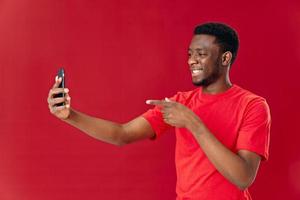 allegro uomo nel un' rosso maglietta con un' Telefono nel il suo mani comunicare emozioni foto