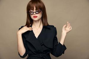 alla moda donna gesti con il suo mani e bicchieri su il suo viso nero cappotto foto
