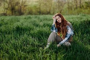 un' giovane bellissimo donna si siede su il verde erba nel il parco e sembra su in il ambientazione sole foto