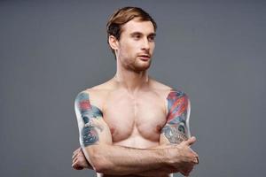 sexy bodybuilder con nudo torso fatto di muscolo tatuaggi grigio sfondo attraversato braccia su il petto foto