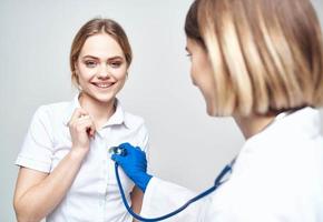 medico con un' stetoscopio e un' contento paziente su un' leggero sfondo foto