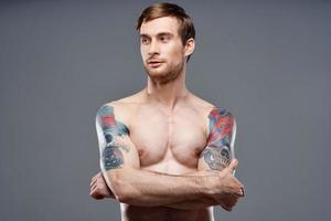 sexy bodybuilder con nudo torso fatto di muscolo tatuaggi grigio sfondo attraversato braccia su il petto foto