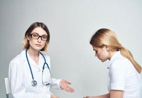 medico si siede su un' sedia e donna paziente in casa su un' leggero sfondo ritagliata Visualizza foto