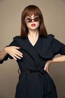 alla moda donna nero cappotto con mani a il vita elegante aspetto beige sfondo foto