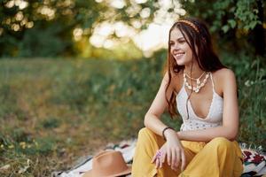 ragazza vestito come un' hippie eco rilassante nel il parco, seduta su un' coperta nel il tramonto, rilassato stile di vita foto