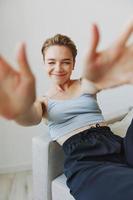 adolescenziale ragazza seduta su il divano a casa sorridente nel casa Abiti e bicchieri con un' corto taglio di capelli, stile di vita senza filtri, gratuito copia spazio foto