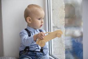un' piccolo bambino sembra su il finestra. il ragazzo con un' giocattolo si siede su un' finestra davanzale. foto