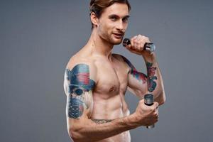 maschio atleta con un' tatuaggio su il suo braccio nudo torso gonfiato muscoli manubri fitness foto