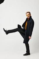 elegante uomo nel un' cappotto buio i pantaloni leggero sfondo bicchieri posa foto