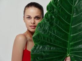 un' donna nel un' rosso costume da bagno sta vicino un' verde foglia di un' palma albero nudo le spalle modello foto