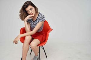 bella donna nel alla moda Abiti seduta su il rosso sedia in posa studio foto
