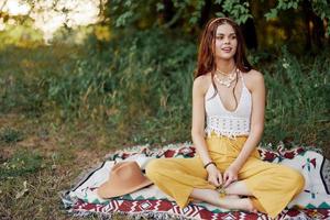 ragazza vestito come un' hippie eco rilassante nel il parco, seduta su un' coperta nel il tramonto, rilassato stile di vita foto