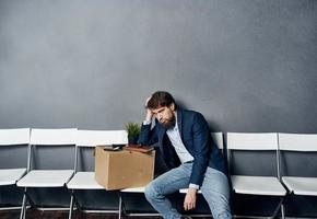 un' uomo nel un' completo da uomo si siede su un' sedia con un' scatola lavoro ricerca depressione foto