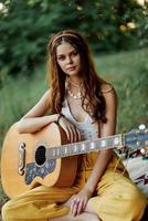 contento hippie donna con un' chitarra sorrisi seduta nel natura di il lago foto