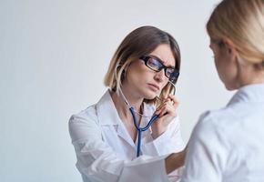 donna pulizia signora nel un' medico toga ascolta per il del paziente battito cardiaco su un' leggero sfondo foto