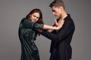 irritato donna nel un' vestito spinge il uomo per il lato contro un' grigio sfondo foto