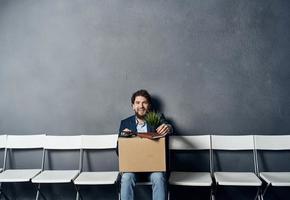 un' uomo con un' scatola si siede su un' sedia con cose documenti licenziamento foto
