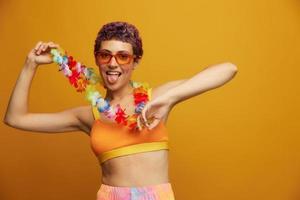 donna con floreale hawaiano ghirlanda in giro sua collo ha divertimento danza e sorridente nel luminosa capi di abbigliamento contro un arancia sfondo foto