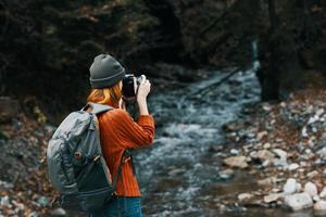 donna con un' telecamera su natura nel il montagne vicino il fiume e alto alberi foresta paesaggio foto