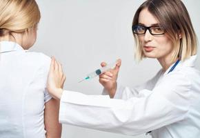 un' donna medico nel un' medico toga è dando un iniezione per un' paziente foto