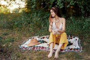 ragazza vestito come un' hippie eco rilassante nel il parco, seduta su un' coperta nel il tramonto, rilassato stile di vita foto