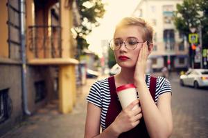 bella donna con bicchieri su il strada camminare un' tazza di caffè foto