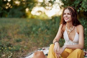 ragazza vestito come un' hippie eco rilassante nel il parco, seduta su un' coperta nel il tramonto, rilassato stile di vita foto