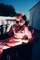 attraente donna rosa vestito si siede su il terrazza soleggiato giorno foto