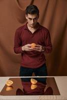 un' bello tipo nel un' camicia sta di età con tagliare arance foto