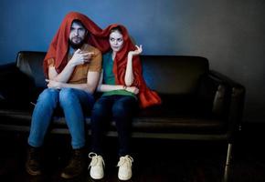 un' donna e un' uomo sotto un' rosso coperta su il divano Guardando tv nel il sera foto