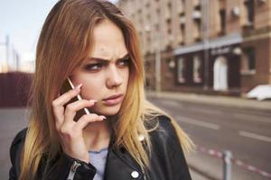 ritagliata Visualizza di bionda donna con mobile Telefono su il strada vicino il edificio foto