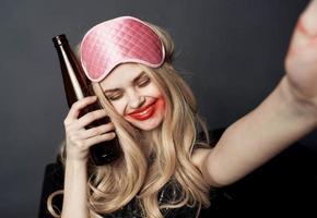 ubriaco donna con un' bottiglia di birra avendo divertimento su un' grigio sfondo e Esprimere a gesti con sua mani foto