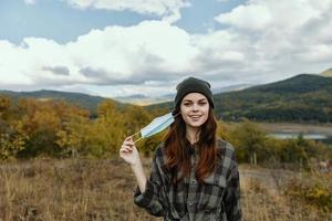 un' donna con un' medico maschera nel sua mano passeggiate nel il parco nel natura foto